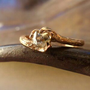 May include: A gold ring with a textured band and a clear gemstone. The band is shaped like a branch.