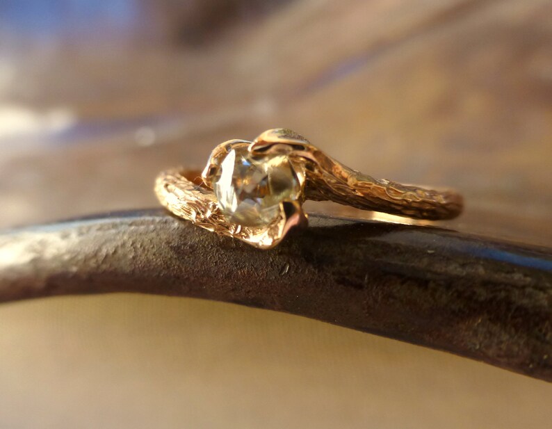 May include: A gold ring with a textured band and a clear gemstone. The band is shaped like a branch.