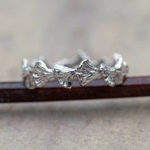 May include: A silver ring with a design of ginkgo leaves. The ring is made of metal and has a polished finish.