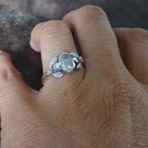 May include: A silver ring with a large oval-shaped clear gemstone surrounded by smaller clear gemstones in a leaf design.