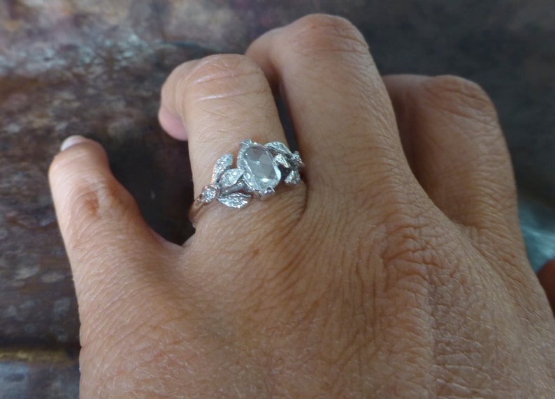 May include: A silver ring with a large oval-shaped clear gemstone surrounded by smaller clear gemstones in a leaf design.