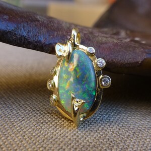 May include: A gold pendant with a green opal gemstone surrounded by small diamonds. The pendant is oval shaped and has a delicate design.