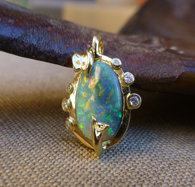 May include: A gold pendant with a green opal gemstone surrounded by small diamonds. The pendant is oval shaped and has a delicate design.