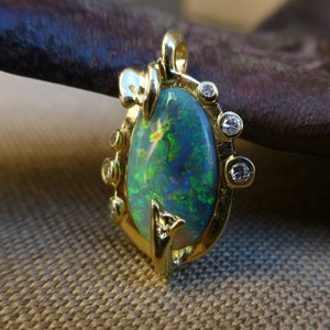 May include: A gold pendant featuring a large oval-shaped green opal surrounded by a delicate gold setting with small diamonds. The pendant has a floral design.