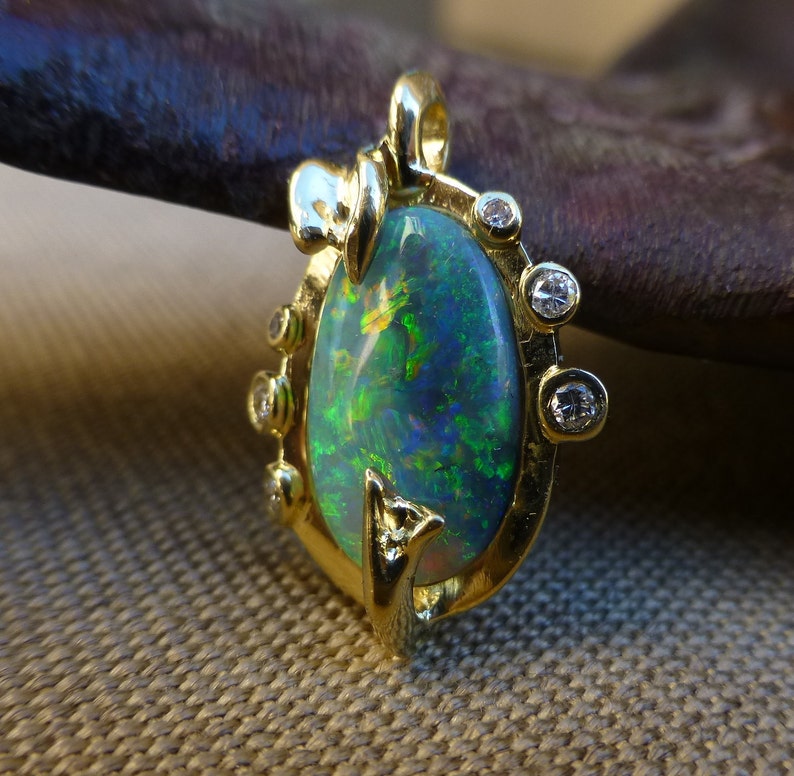 May include: A gold pendant featuring a large oval-shaped green opal surrounded by a delicate gold setting with small diamonds. The pendant has a floral design.