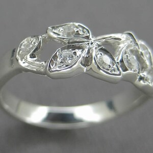 Puede incluir: Un anillo de plata con un delicado dise&ntilde;o de cinco hojas, cada una con una peque&ntilde;a piedra clara engastada en el centro.
