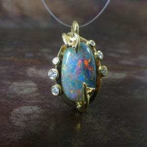 May include: A gold pendant featuring a large oval opal with iridescent blue, green, and red hues. The opal is surrounded by a gold setting with small diamonds.