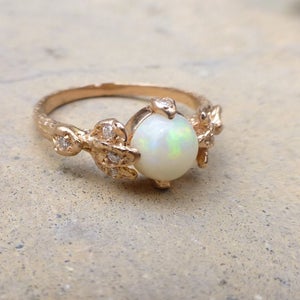 May include: A gold ring with a white opal gemstone and small diamonds set in a delicate leaf design.