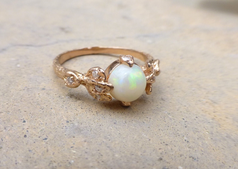 May include: A gold ring with a white opal gemstone and small diamonds set in a delicate leaf design.