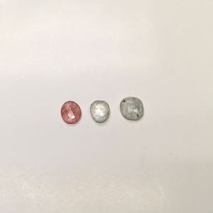 May include: Three oval-shaped gemstones. One is pink, one is white, and one is gray.