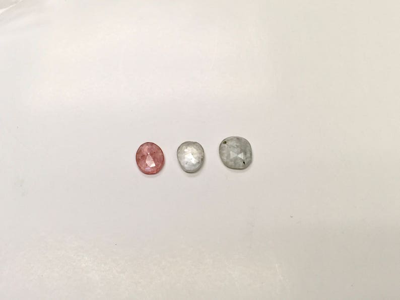 May include: Three oval-shaped gemstones. One is pink, one is white, and one is gray.