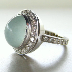 May include: A silver ring with a large, light blue gemstone surrounded by a halo of smaller, clear gemstones.