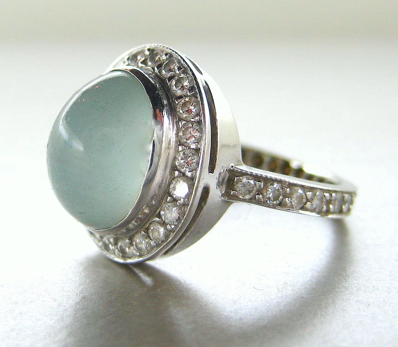 May include: A silver ring with a large, light blue gemstone surrounded by a halo of smaller, clear gemstones.