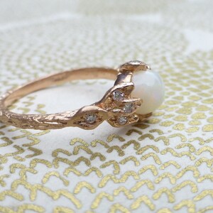 May include: A rose gold ring with a white opal gemstone and small diamonds set in a delicate, textured band.