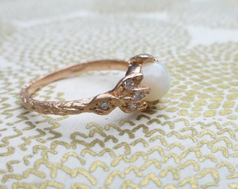May include: A rose gold ring with a white opal gemstone and small diamonds set in a delicate, textured band.