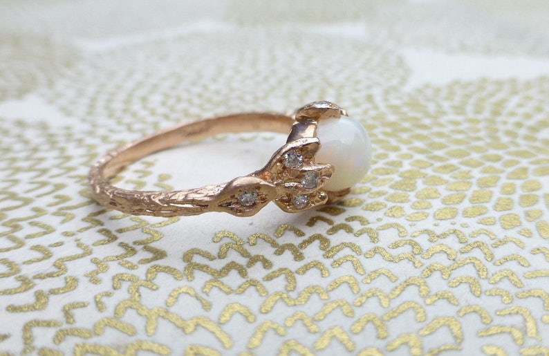 May include: A rose gold ring with a white opal gemstone and small diamonds set in a delicate, textured band.