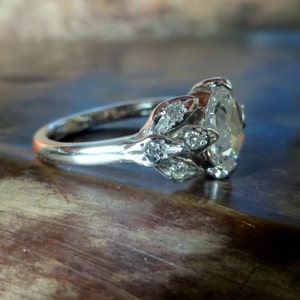 May include: A silver engagement ring with a large oval-shaped diamond surrounded by smaller diamonds set in a leaf-like design.