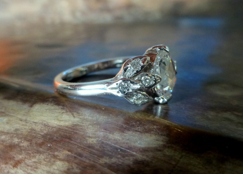May include: A silver engagement ring with a large oval-shaped diamond surrounded by smaller diamonds set in a leaf-like design.
