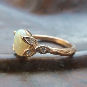 May include: A gold ring with a white opal gemstone and small diamonds set in a leaf design.