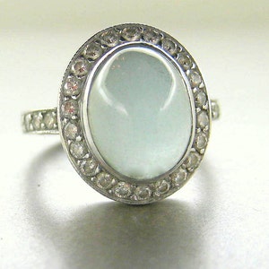 May include: A silver ring with a large oval-shaped light blue gemstone surrounded by a halo of smaller clear gemstones.