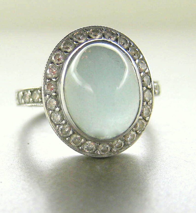May include: A silver ring with a large oval-shaped light blue gemstone surrounded by a halo of smaller clear gemstones.