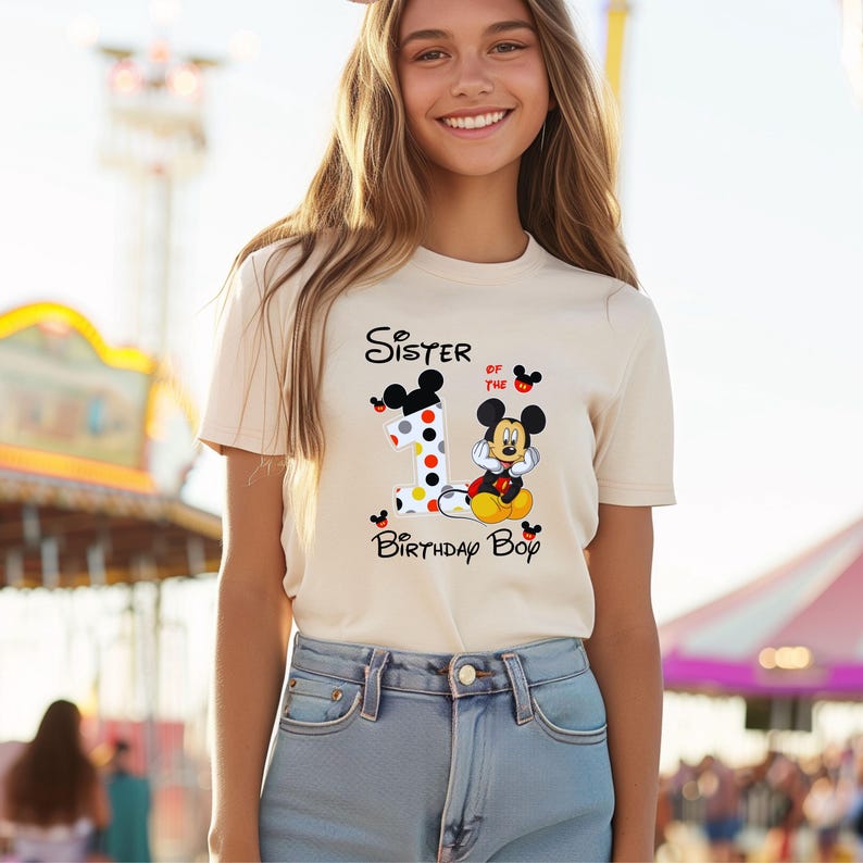 以下が含まれることがあります： ミッキーマウスのグラフィックと「Sister of the Birthday Boy」の文字が入ったクリーム色のTシャツ。数字の「1」は水玉模様で装飾されています。ミッキーマウスは赤いショートパンツと黄色の靴を履いています。