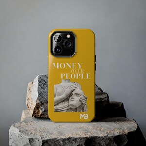 Könnte beinhalten: Senfgelbe Handyhülle mit dem Text "MONEY OVER PEOPLE" in Weiß. Die Hülle zeigt eine Grafik einer klassischen Statue, die eine Maske hält. Die Hülle liegt auf einer grauen Steinoberfläche.