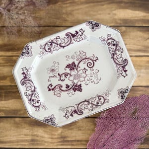 May include: An octagonal ceramic serving platter featuring a cream-colored base with a dark purple floral transferware pattern. The design includes intricate scrolling vines and blossoms centered on the platter, with matching decorative borders.