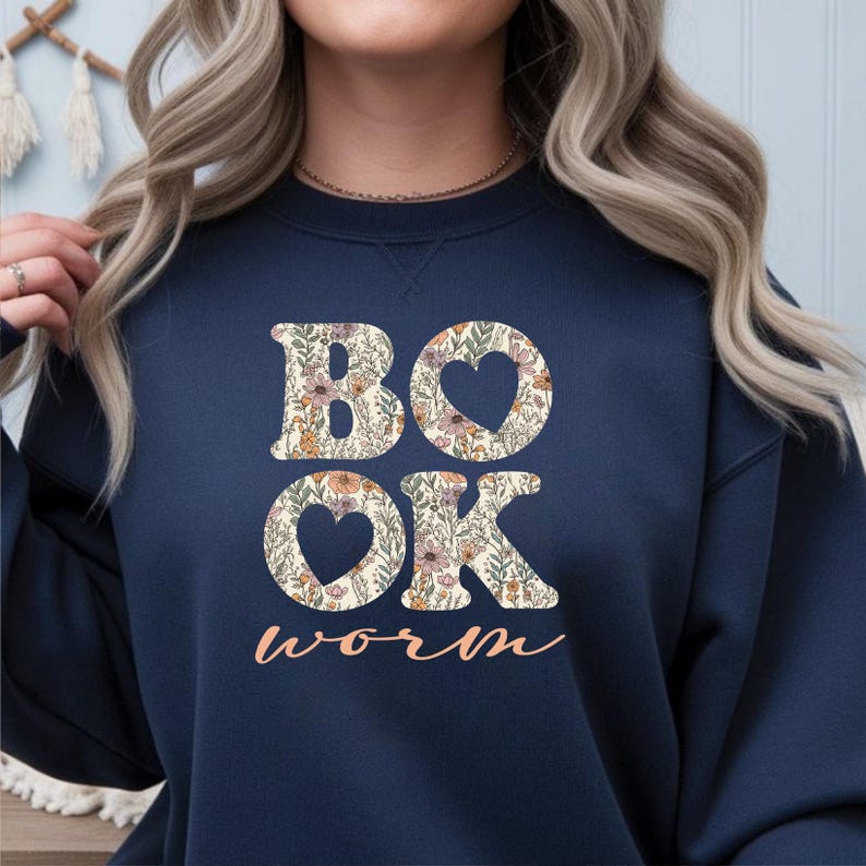 May include: Navy blue sweatshirt with the words "BOOK WORM" in a floral design. The letters "BO" and "OK" are filled with flowers and leaves, with heart-shaped cutouts. The word "worm" is in a cursive font.