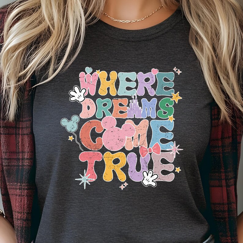 May include: A dark gray t-shirt with a colorful graphic design that says "Where Dreams Come True". The graphic includes Mickey Mouse ears, a castle, stars, and other Disney-themed elements.