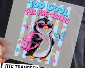 May include: A DTF transfer featuring a penguin wearing pink sunglasses and a pink backpack, with the text "TOO COOL FOR PRE-SCHOOL" in blue and pink. The design includes colorful butterflies, stars, and hearts against light blue vertical stripes.