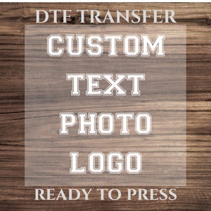 May include: A clear sheet with the text "DTG Transfer", "Custom Text", "Photo", and "Logo" in a white, bold, block font. The text is on a woodgrain background with the words "Ready to Press" below the sheet.