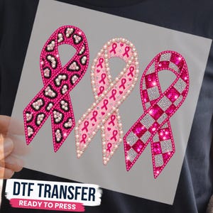May include: A DTF transfer sheet featuring three awareness ribbons. The left ribbon has a pink and black leopard print. The center ribbon is light pink with small pink ribbon icons and pearl borders. The right ribbon has a pink and silver checkerboard pattern.