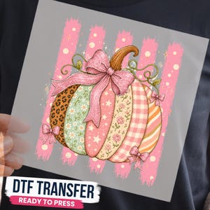 May include: A DTF transfer featuring a pumpkin graphic with vertical segments in leopard print, floral, star, rose, gingham, and striped patterns. The pumpkin is adorned with a large glittery pink bow and smaller bows, set against a background of pink brushstrokes.