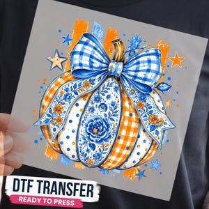 May include: A DTF transfer featuring a pumpkin graphic with orange gingham and white polka dot sections, decorated with a large blue and white gingham bow. The design includes blue floral patterns, orange flowers, and blue stars on a gray background.