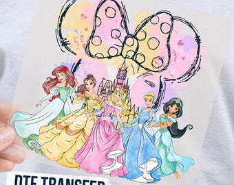 May include: A DTF transfer sheet featuring a colorful graphic of five animated princesses standing before a castle silhouette, topped with a large polka-dot bow outline and watercolor splashes in pink, yellow, and blue hues.