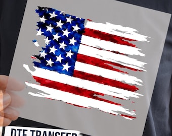 May include: A DTF transfer sheet featuring a distressed, brushstroke-style American flag graphic in red, white, and blue. The design includes a blue canton with white stars and horizontal red and white stripes. Text at the bottom reads DTF TRANSFER READY TO PRESS.