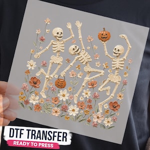May include: A DTF transfer featuring three off-white skeletons dancing among a field of colorful flowers in shades of orange, pink, and white. One skeleton holds an orange jack-o'-lantern bucket, and another holds a small orange pumpkin.