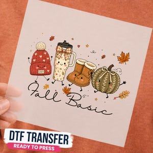 Peut inclure: Une feuille de transfert DTF avec une illustration de dessin animé représentant un bonnet rouge, un gobelet à motifs avec un nœud, des bottes marron et une citrouille verte, tous souriants. Le texte "Fall Basic" est écrit en cursif noir.