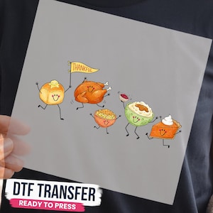 Peut inclure: Un transfert DTF présentant une illustration de dessin animé d'aliments de Thanksgiving avec des visages souriants, dont un petit pain beurré tenant un drapeau jaune avec l'inscription THANKFUL, une dinde rôtie, des macaronis au fromage, de la purée et une tarte à la citrouille.