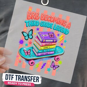 May include: A DTF transfer sheet featuring a graphic with the text BRB BECOMING A THIRD GRADE LEGEND. The design includes a stack of colorful books on a teal skateboard, surrounded by butterflies, stars, and lightning bolts in vibrant colors.