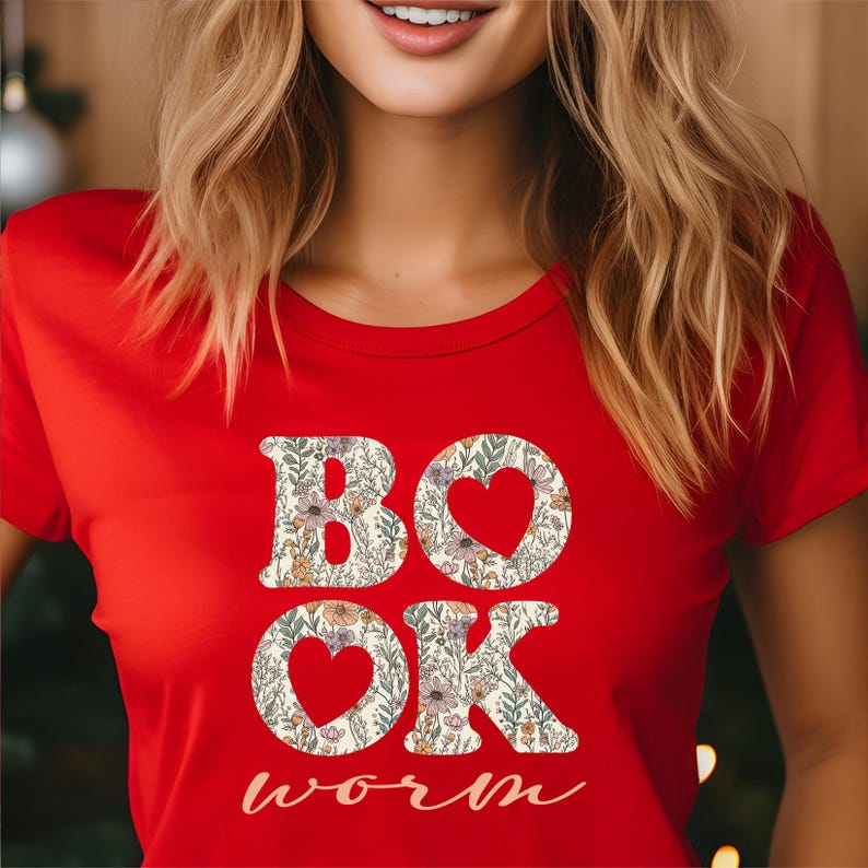 May include: A red t-shirt with the words "BOOK" and "OK" in a floral pattern, with heart-shaped cutouts in the "O"s. The word "worm" is written in cursive below. The shirt is a crew neck.