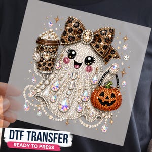 May include: A DTF transfer featuring a ghost covered in white rhinestones, wearing a leopard print bow, holding a leopard print coffee cup and an orange jack-o'-lantern bucket. The design is accented with iridescent teardrop gems, pearls, and gold stars.