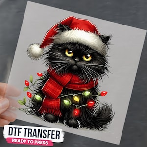 May include: A DTF transfer featuring a fluffy black cat wearing a red Santa hat and a red plaid scarf. The cat is wrapped in a string of colorful Christmas lights. The text at the bottom reads DTF TRANSFER READY TO PRESS in bold black letters.