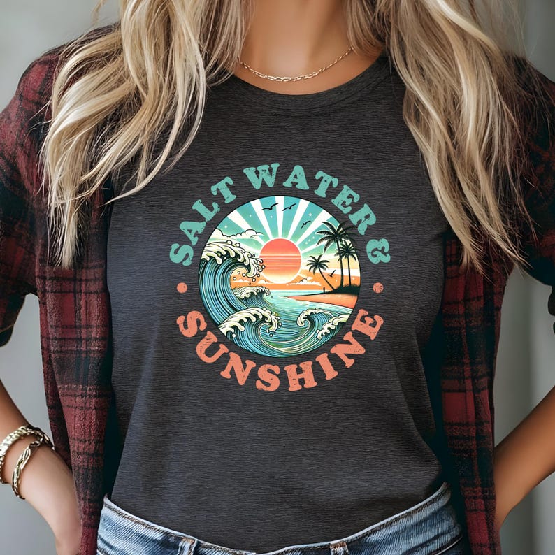 May include: A dark gray t-shirt with a vintage-style graphic of a sunset over the ocean with waves crashing. The graphic is surrounded by the text "Salt Water & Sunshine".