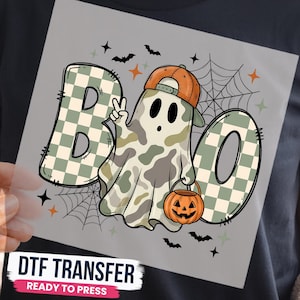 May include: A DTF transfer featuring the text BOO with a checkered pattern in sage green and white. A ghost character wears an orange baseball cap, makes a peace sign, and holds an orange jack-o'-lantern bucket. Includes spiderwebs, bats, and stars.