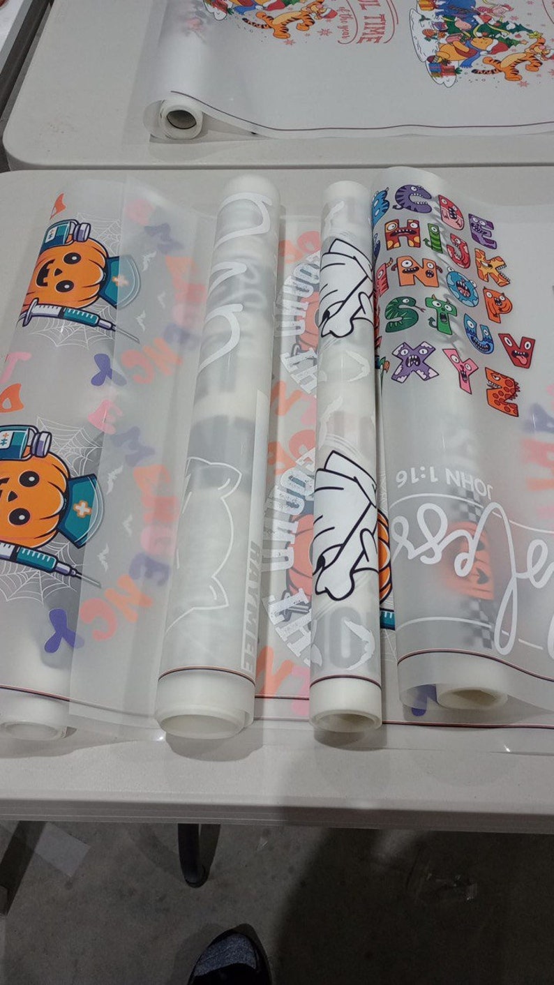 May include: Four rolls of clear vinyl with different designs printed on them. The designs include a pumpkin with a syringe, a ghost, a hand with a basketball, and a colorful alphabet.