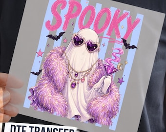 May include: A DTF transfer featuring a ghost wearing heart-shaped purple sunglasses, a layered gold necklace, and a fluffy purple coat. The ghost holds a purple martini glass. The text SPOOKY appears in pink above, with bats and stars on a blue striped background.