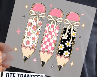 May include: A DTF transfer sheet featuring three pencils with pink erasers and white bows. The first pencil has a pink floral pattern, the second a pink and white checkerboard pattern, and the third a black background with white daisies, surrounded by stars.