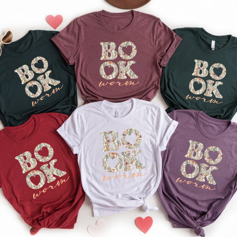 May include: A collection of six short-sleeved t-shirts in various colors, including dark green, burgundy, white, red, and purple. Each shirt features the text "BOOK WORM" in a floral design.